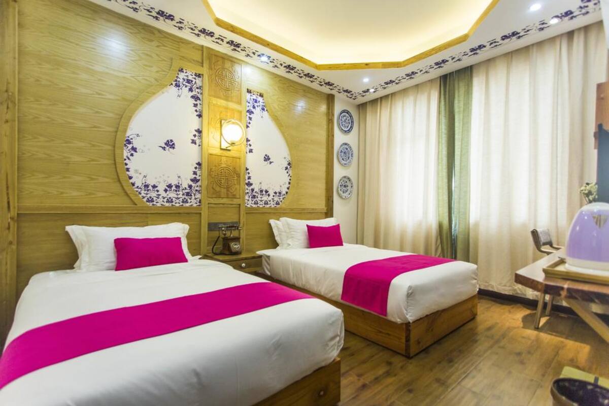 A hotel room with two beds, wooden headboard, decorative wall panels, and a small table with a chair.