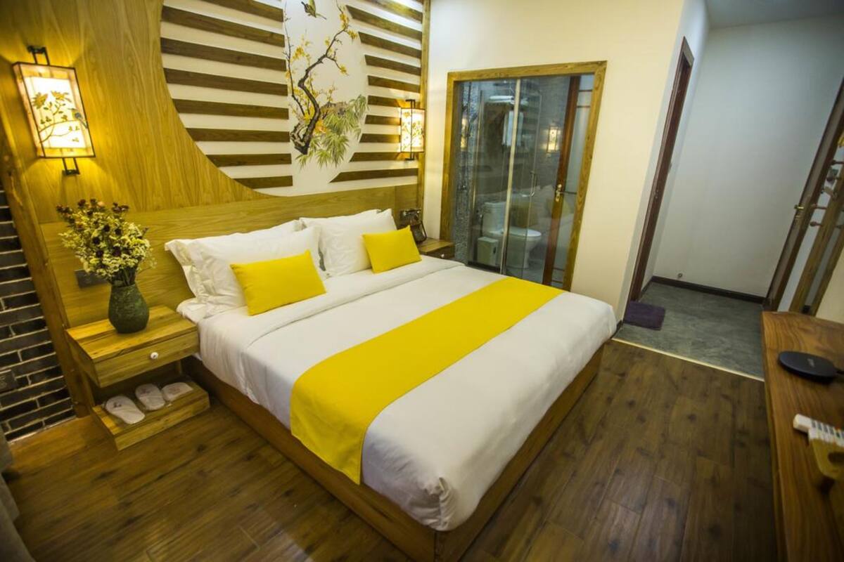A hotel room with a large bed, wooden headboard, and a sliding glass door leading to a balcony.