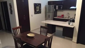 A compact kitchen with dark cabinetry, a microwave, and a refrigerator. There is a dining table with four chairs and a bowl on it.