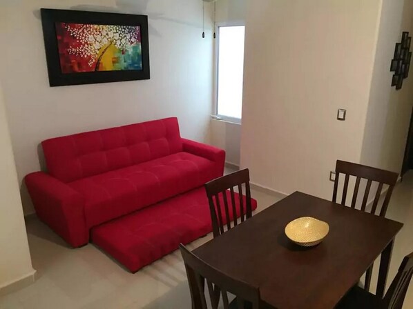 Une pièce avec un canapé rouge, une table à manger entourée de chaises et un tableau coloré accroché au mur.