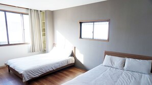 Een slaapkamer met twee bedden, houten vloeren en een raam met gordijnen.