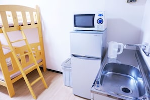 Una kitchenette compacta con microondas, refrigerador, pileta y una silla de madera.