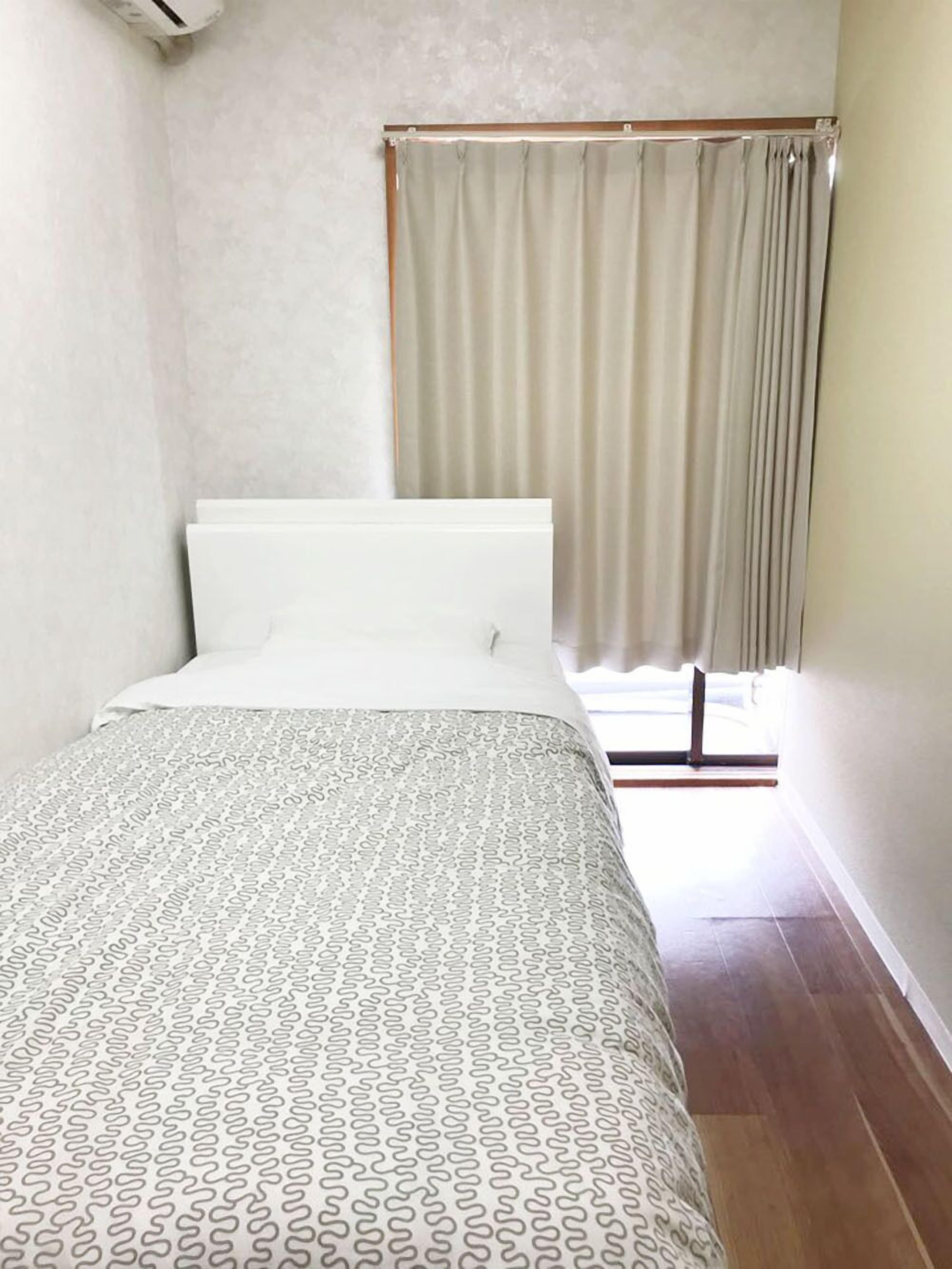 A bedroom with a bed, a window with curtains, and a wooden floor.