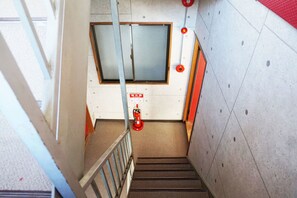 Una escalera con un extintor, una luz de emergencia roja y una puerta con ventanal.