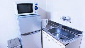 Een kleine kitchenette met een magnetron, koelkast, wastafel en een klein prullenbakje.