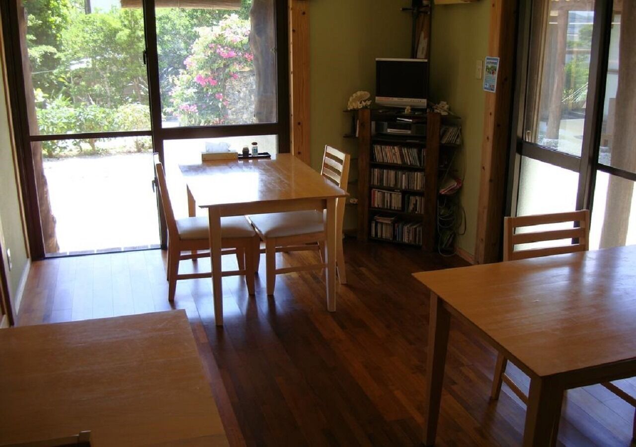 A room with a wooden table and chairs, a bookshelf, and a window with a view of greenery.