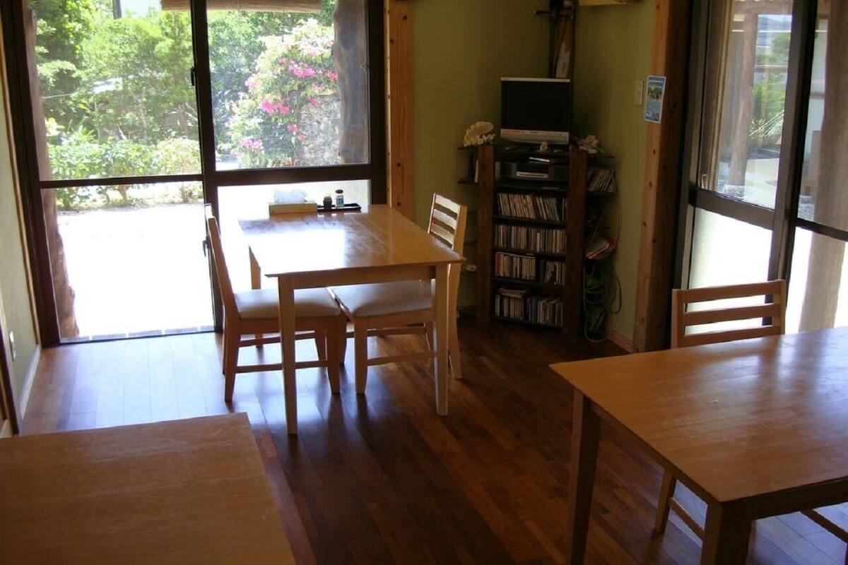 A room with a wooden table and chairs, a bookshelf, and a window with a view of greenery.