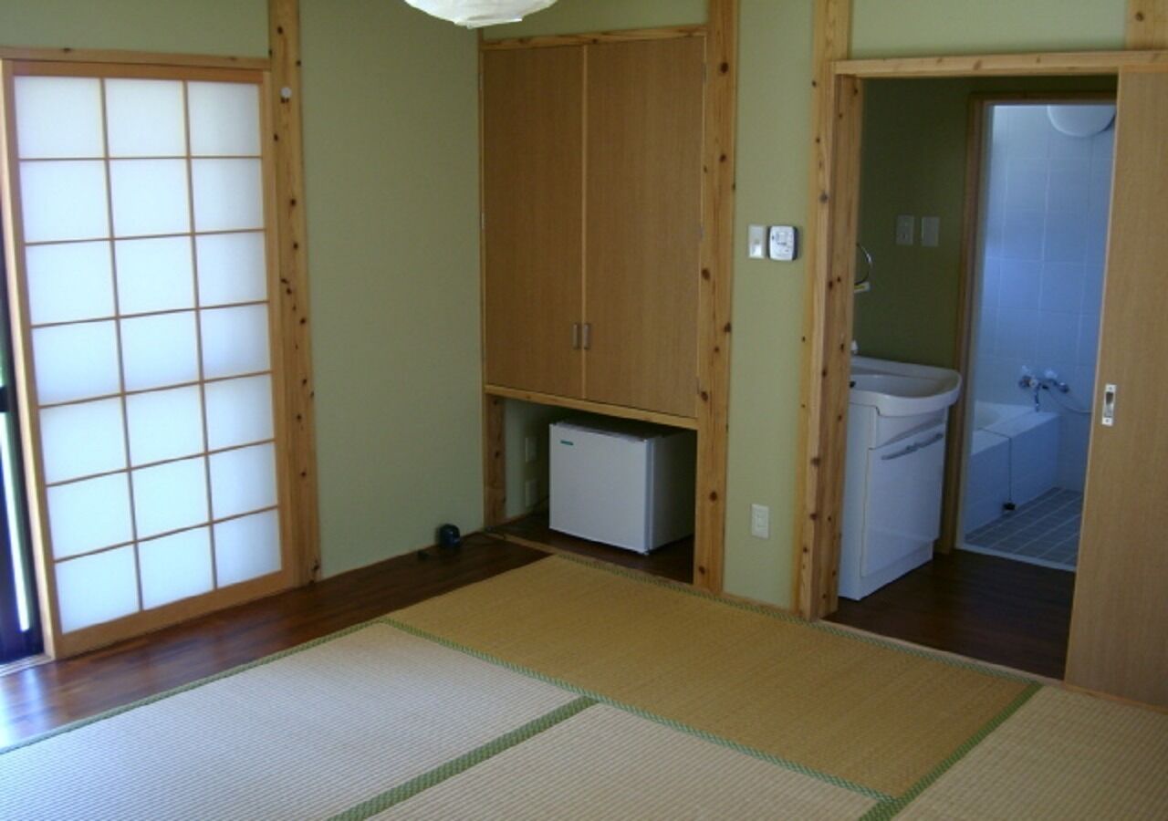 A traditional Japanese room with tatami flooring, a sliding door, a wardrobe, and a small white refrigerator.