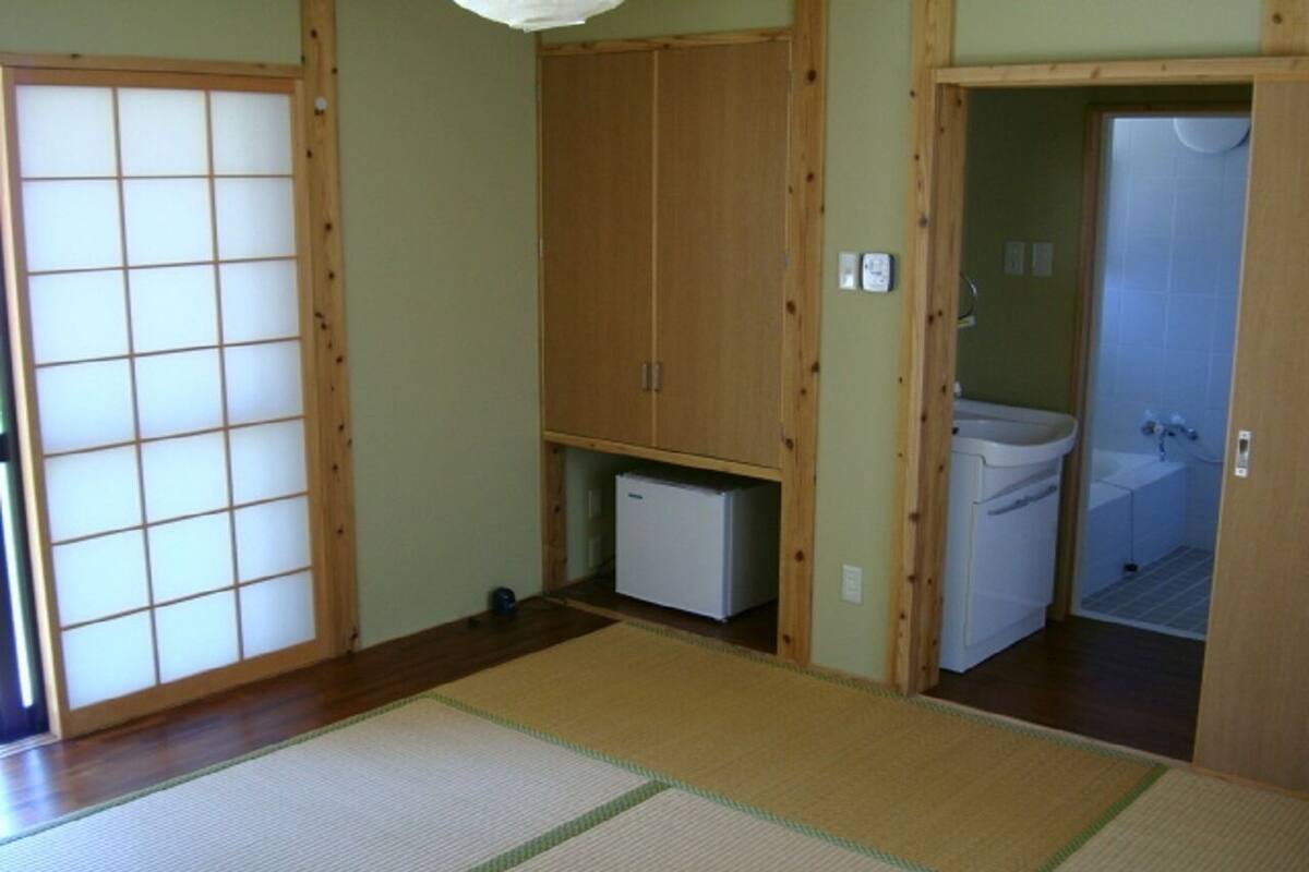 A traditional Japanese room with tatami flooring, a sliding door, a wardrobe, and a small white refrigerator.