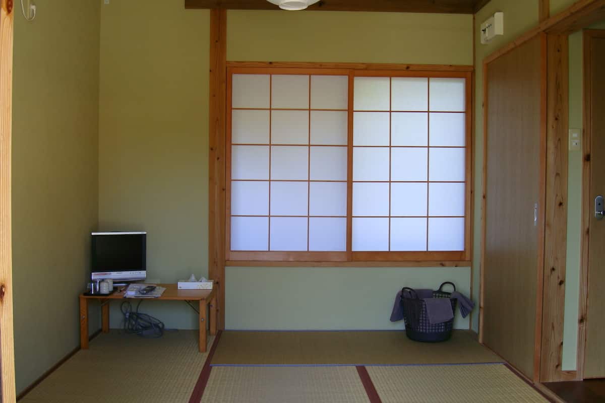 A traditional Japanese room with tatami flooring, a shoji screen window, a desk with a computer, and a futon bed.