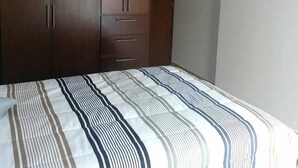 A bedroom with a large wardrobe, a bed with striped bedding, and a plain wall. - Depa Torre Marina (Mazatlán)