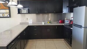 A kitchen with dark cabinets, a stainless steel refrigerator, a gas stove, and a microwave. - Condominio Malecon (Mazatlán)