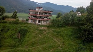 A multi-story building with a flat roof, surrounded by lush greenery and mountains in the background. - 360 Lakefront Restro and Lodge (Pokhara)