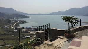 A view of a lake with a stone staircase leading down to the water, surrounded by greenery and a few buildings in the distance. - 360 Lakefront Restro and Lodge (Pokhara)