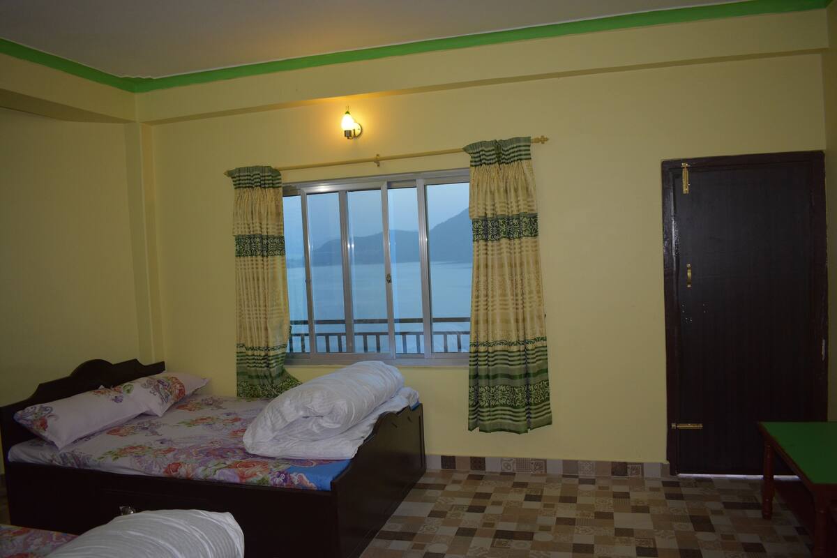 A bedroom with a bed, a window with curtains, a door, and a view of mountains.