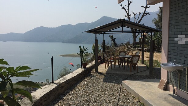 A patio area with a table and chairs, overlooking a body of water and hills. - 360 Lakefront Restro and Lodge (Pokhara)