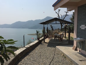A patio area with a table and chairs, overlooking a body of water and hills. - 360 Lakefront Restro and Lodge (Pokhara)