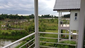A balcony with a view of a river and greenery, a small building with a tiled roof, and a metal railing. - Baansuan Keb Tawan Resort (Lop Buri)