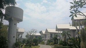 A pathway leading to a row of white buildings with tiled roofs, surrounded by greenery and a clear sky. - Baansuan Keb Tawan Resort (Lop Buri)