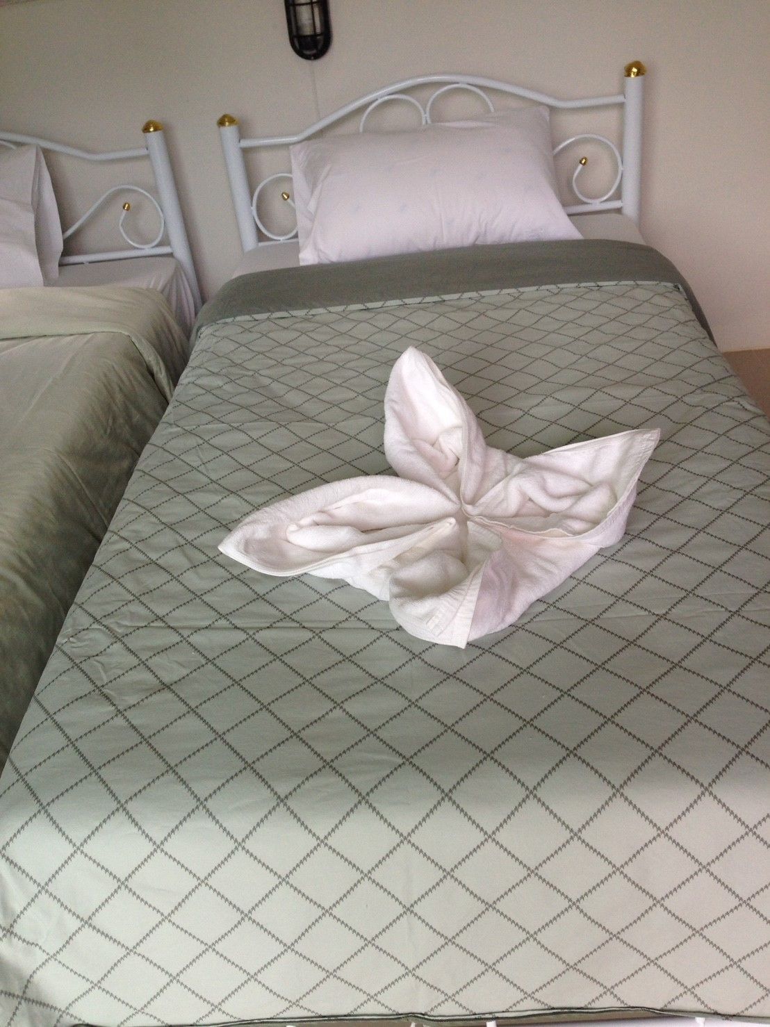 A bed with a quilted green and white bedspread, a white pillow, and a decorative flower arrangement on the bed.