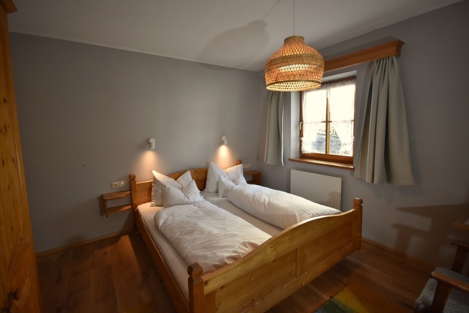 A wooden bed with white bedding in a room with a window and a hanging light fixture.