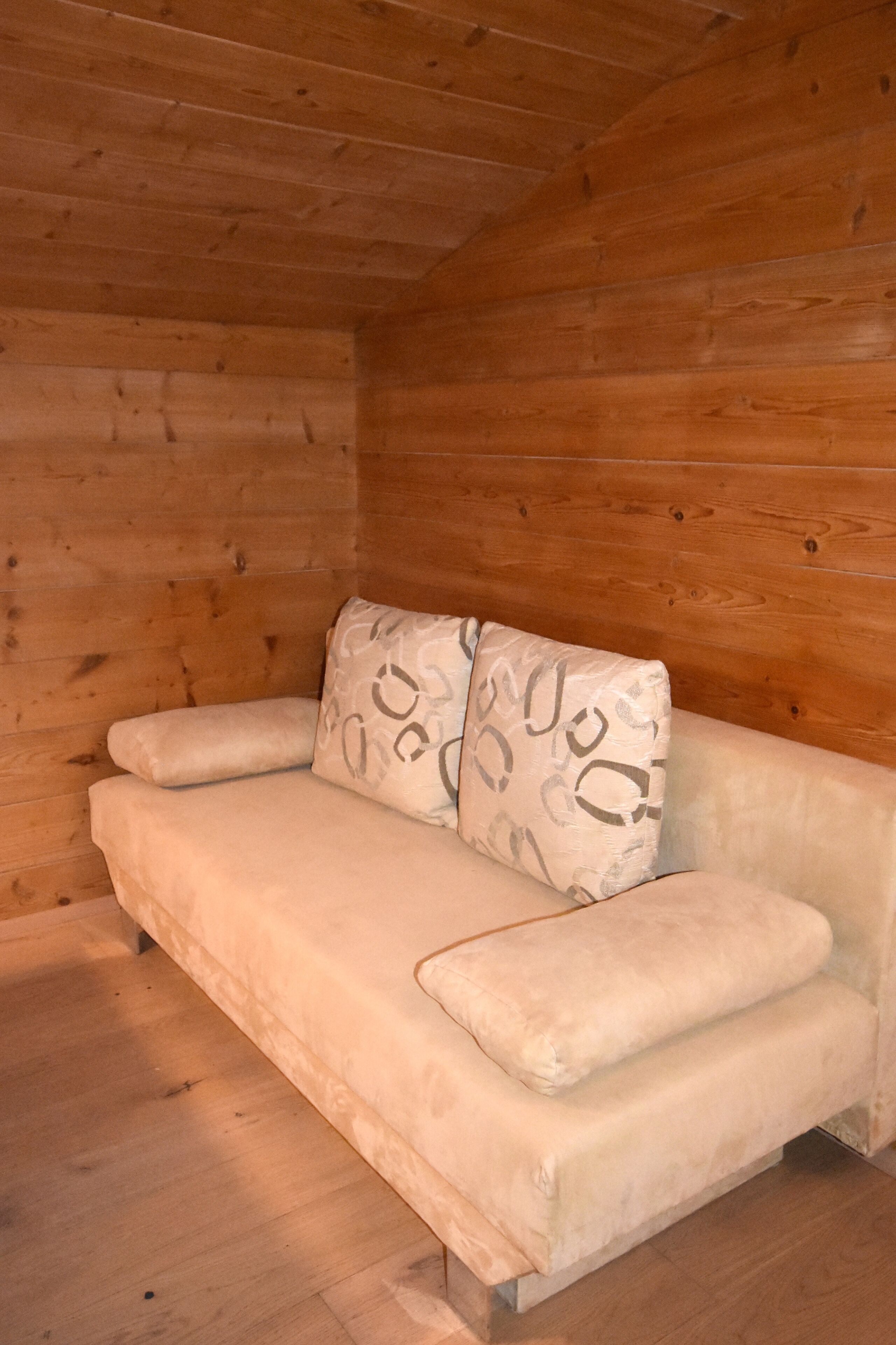 A wooden interior with a beige sofa and patterned cushions.