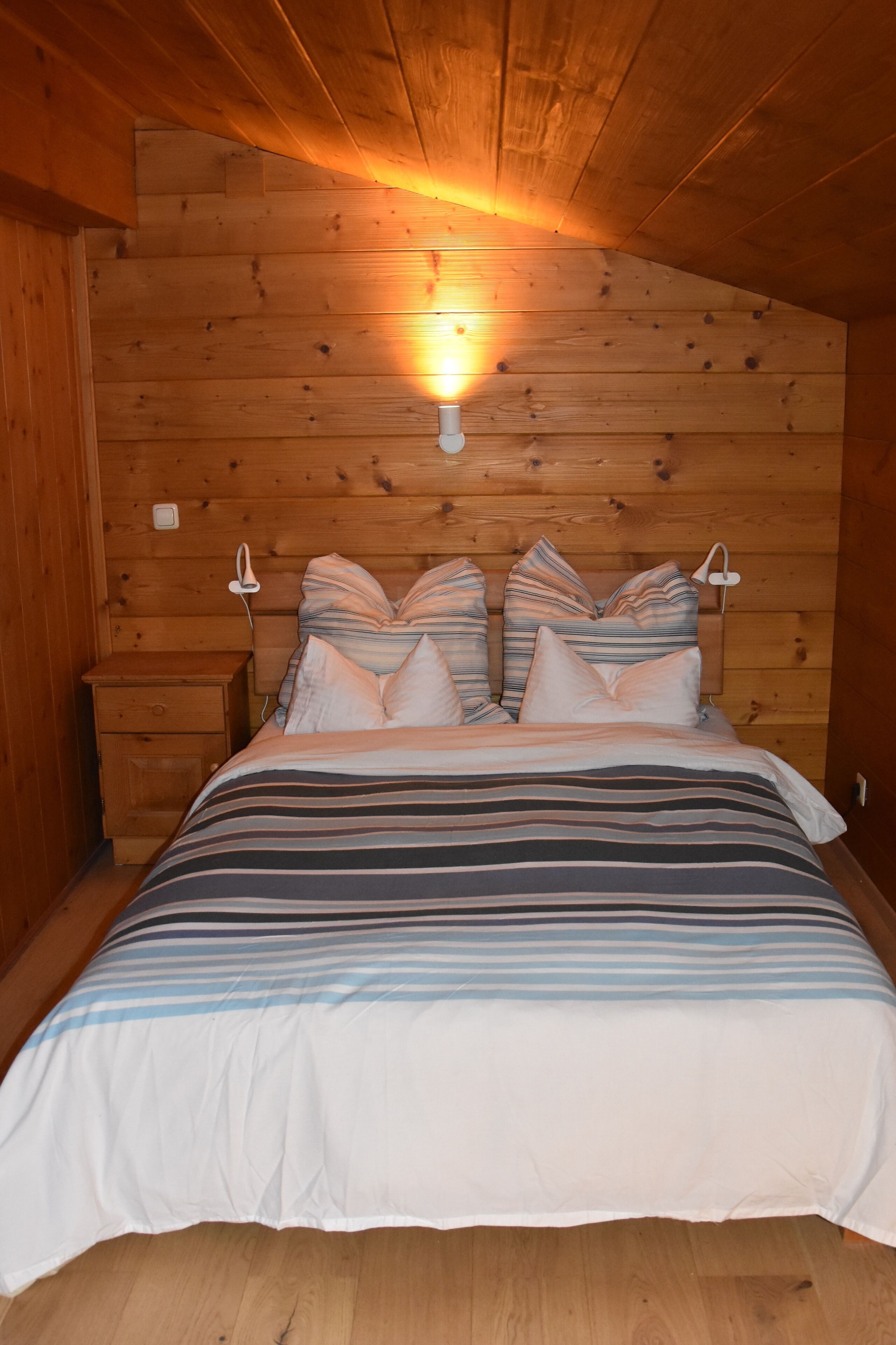A wooden cabin bedroom with a bed, pillows, and a nightstand.