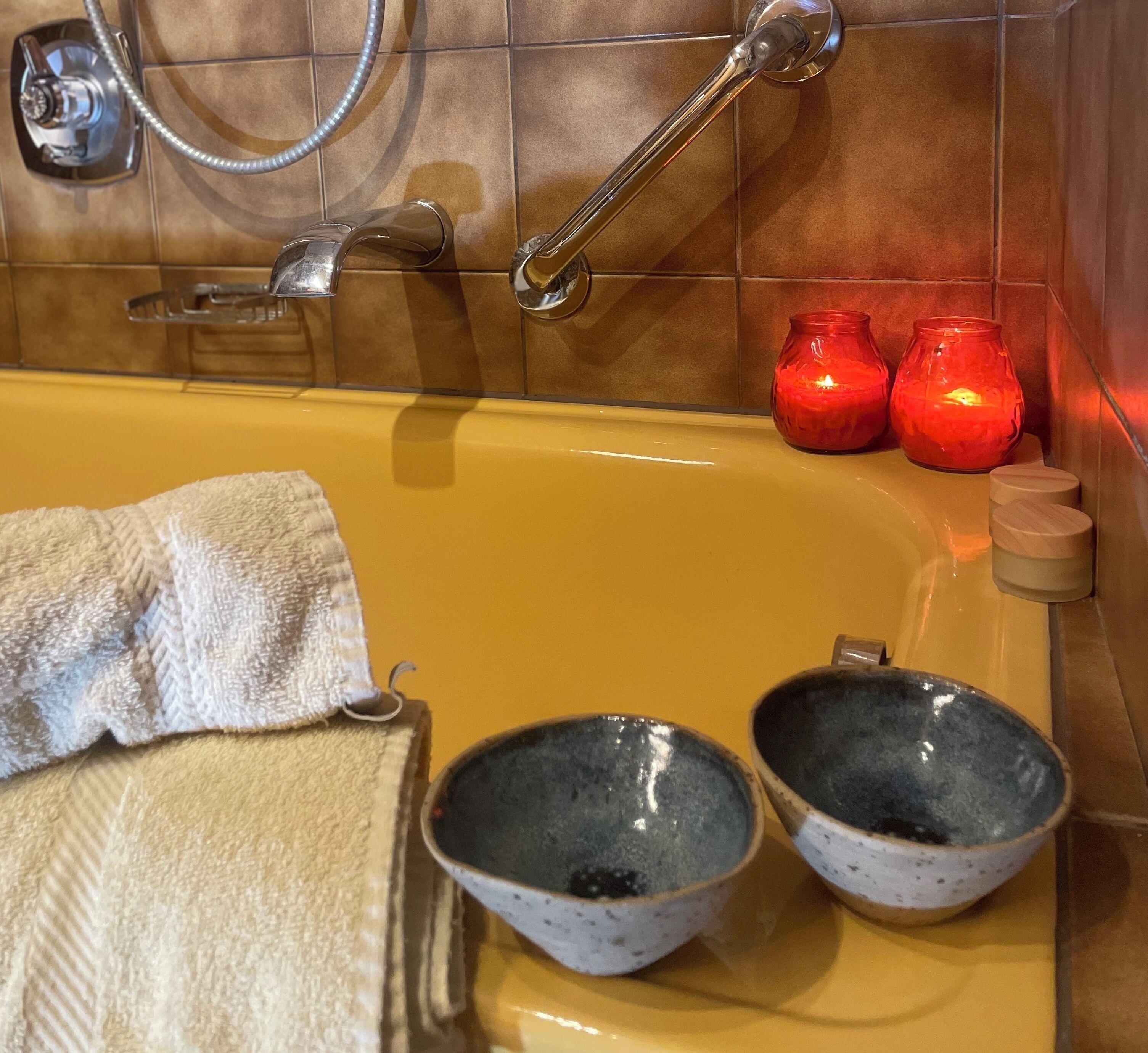 Un baño con bañera, dos lavabos, una toalla y dos velas rojas.