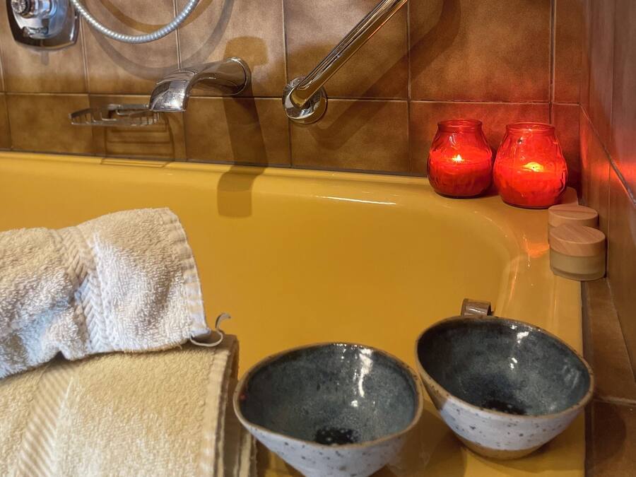 Un baño con bañera, dos lavabos, una toalla y dos velas rojas.