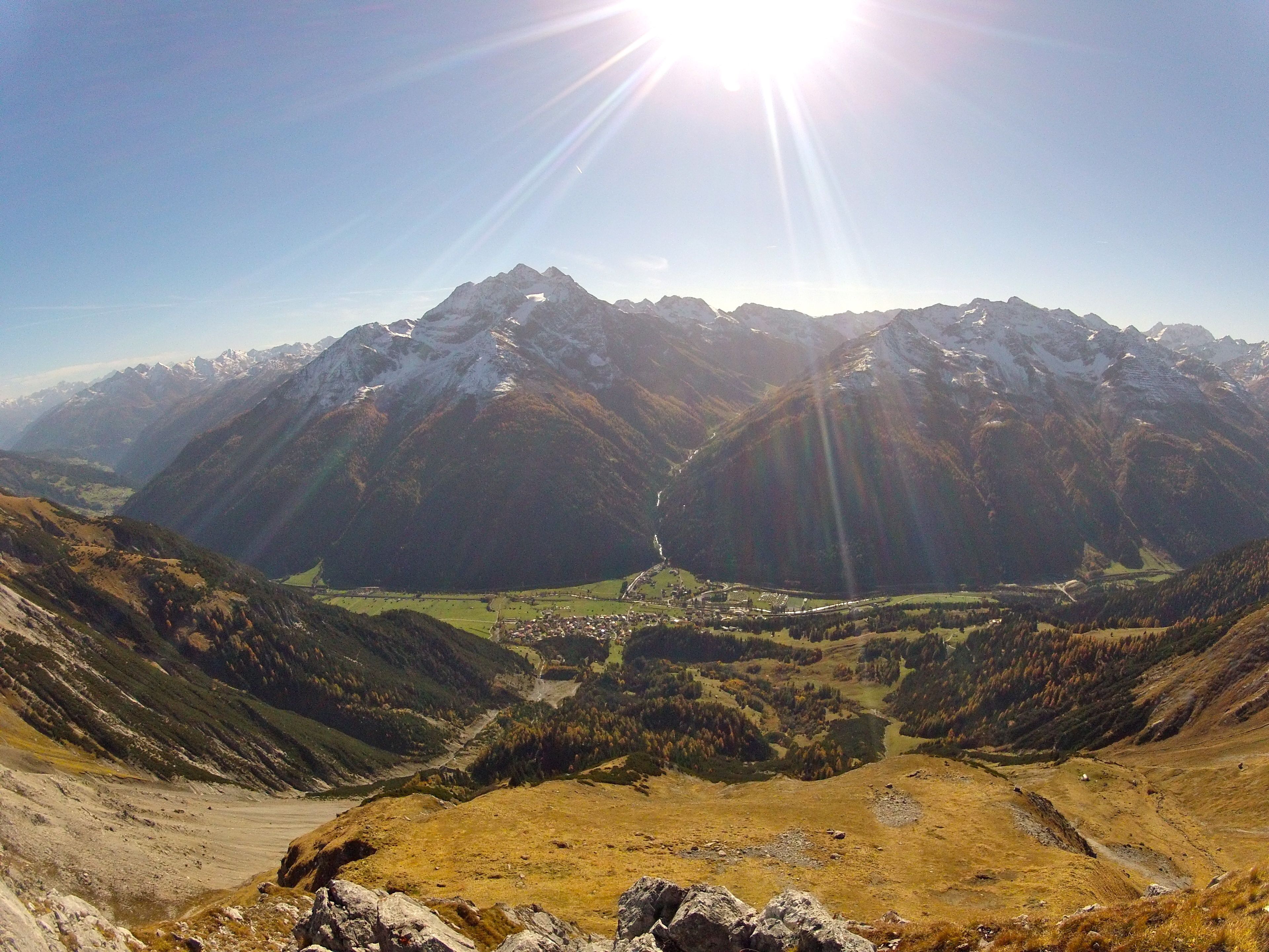 A mountainous landscape with a valley, a small settlement, and a clear sky.