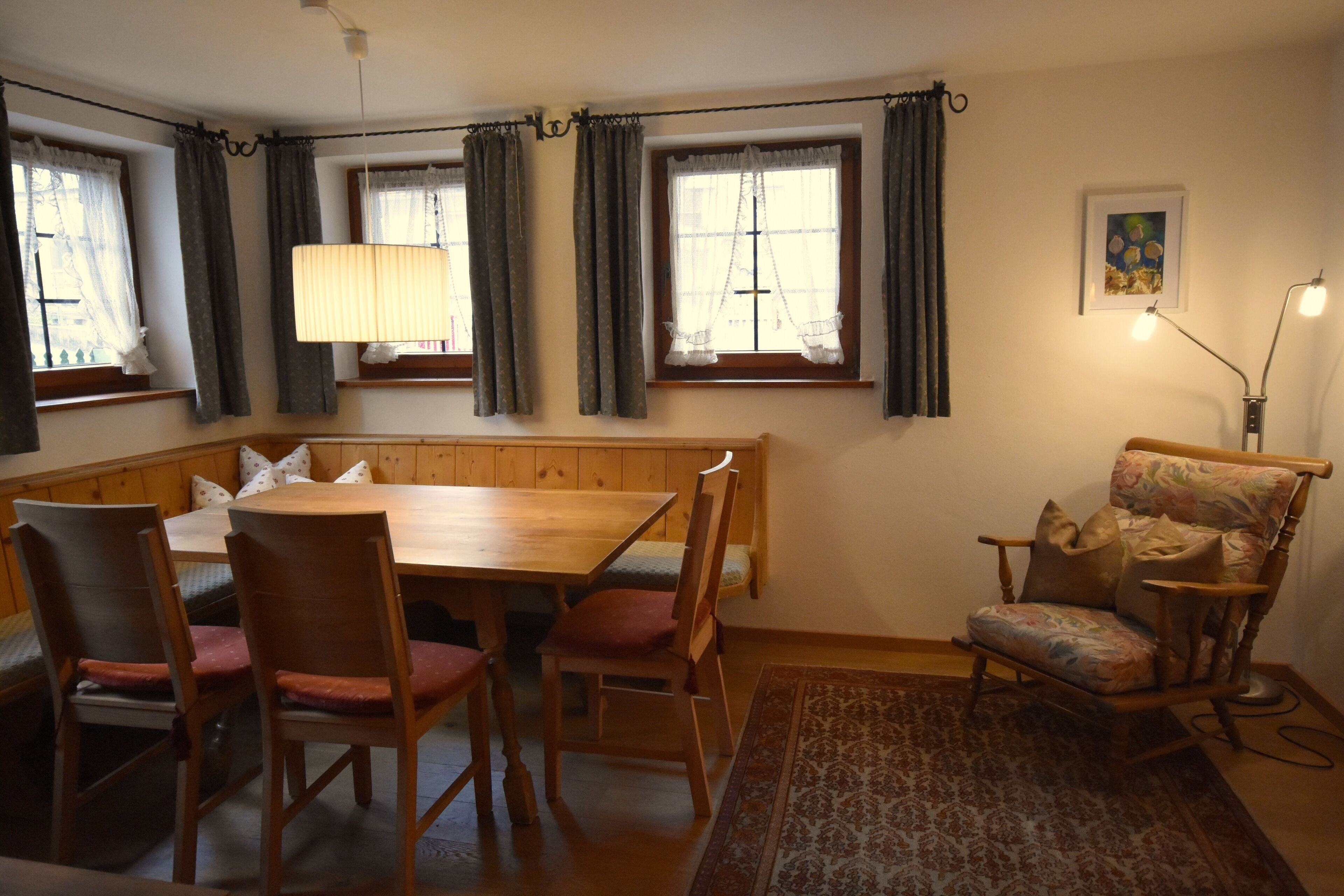 A dining area with a wooden table and chairs, a bench, a patterned rug, and a lamp.