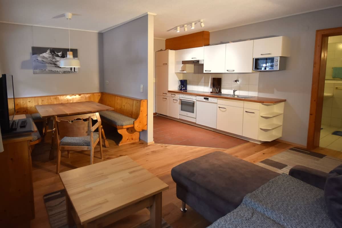 A compact living space with a kitchenette, a dining area with a wooden table and chairs, and a sofa.