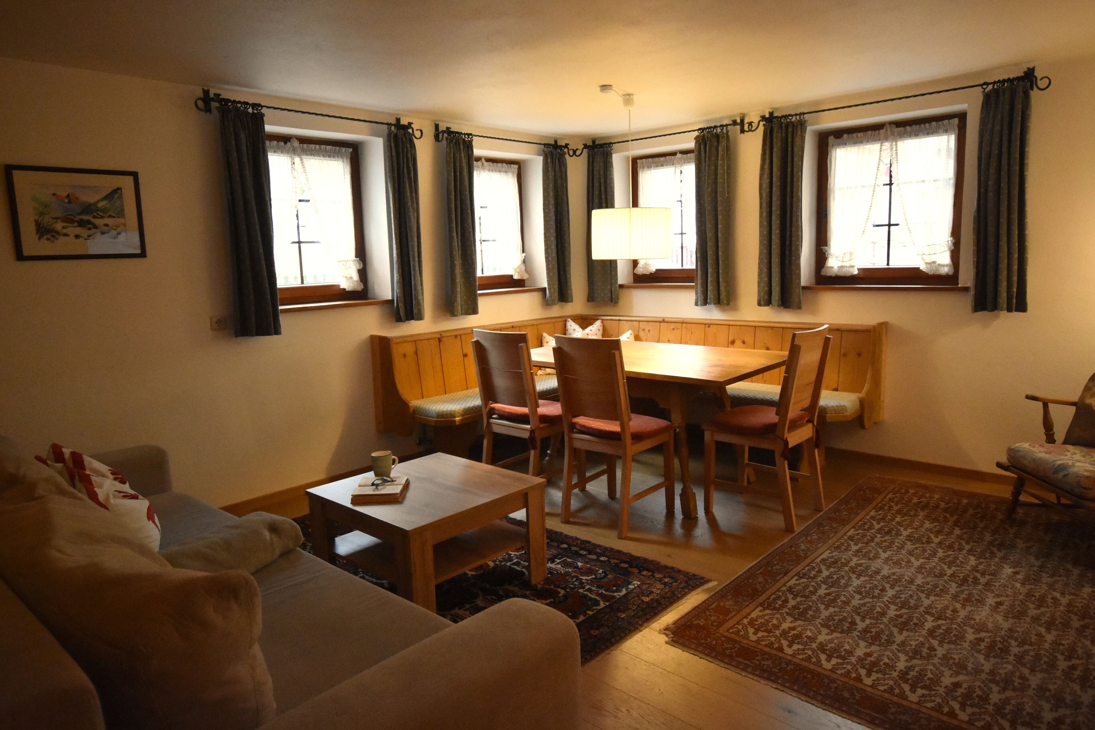 A cozy living room with a wooden dining table, chairs, a sofa, and a patterned rug.
