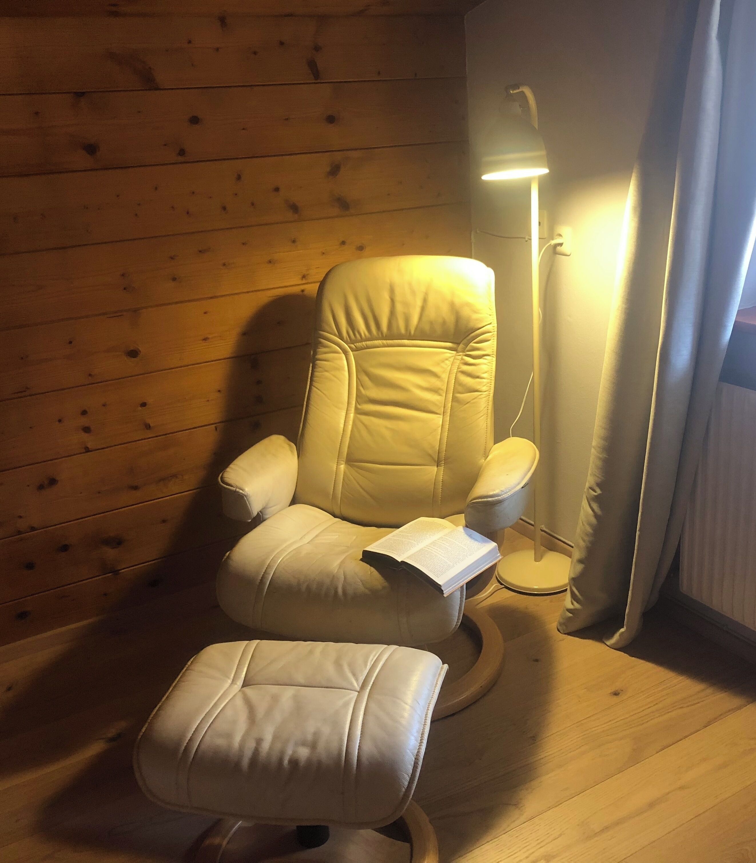Ein Massagesessel mit Fußstütze, vor einer Holzwand, in der Nähe steht eine Stehlampe.