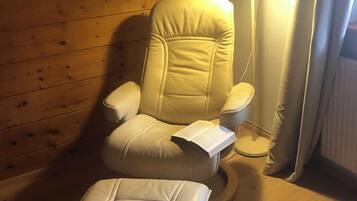 Ein Massagesessel mit Fußstütze, vor einer Holzwand, in der Nähe steht eine Stehlampe.