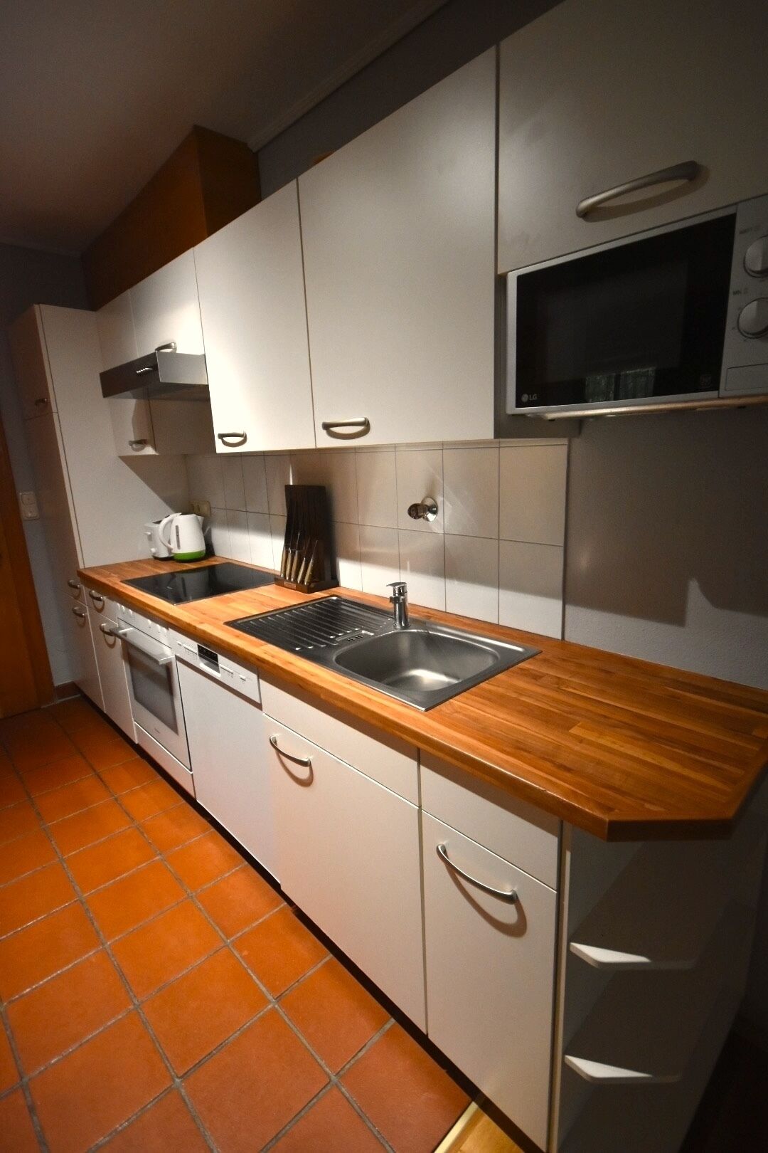 Una cocina moderna con armarios blancos, encimera de madera, pileta de acero inoxidable y microondas.