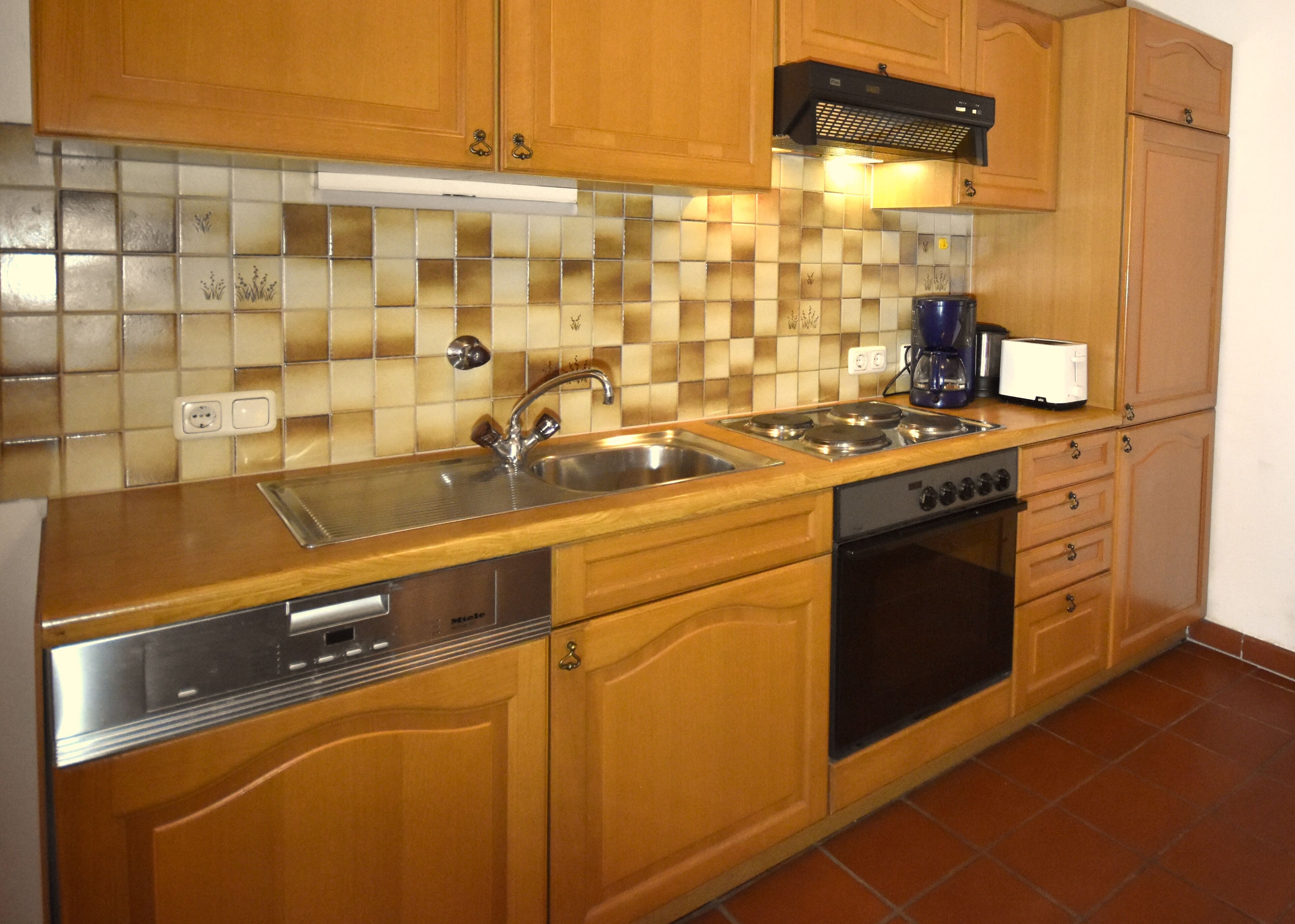 A kitchen with wooden cabinets, a stainless steel sink, a coffee maker, and a toaster.