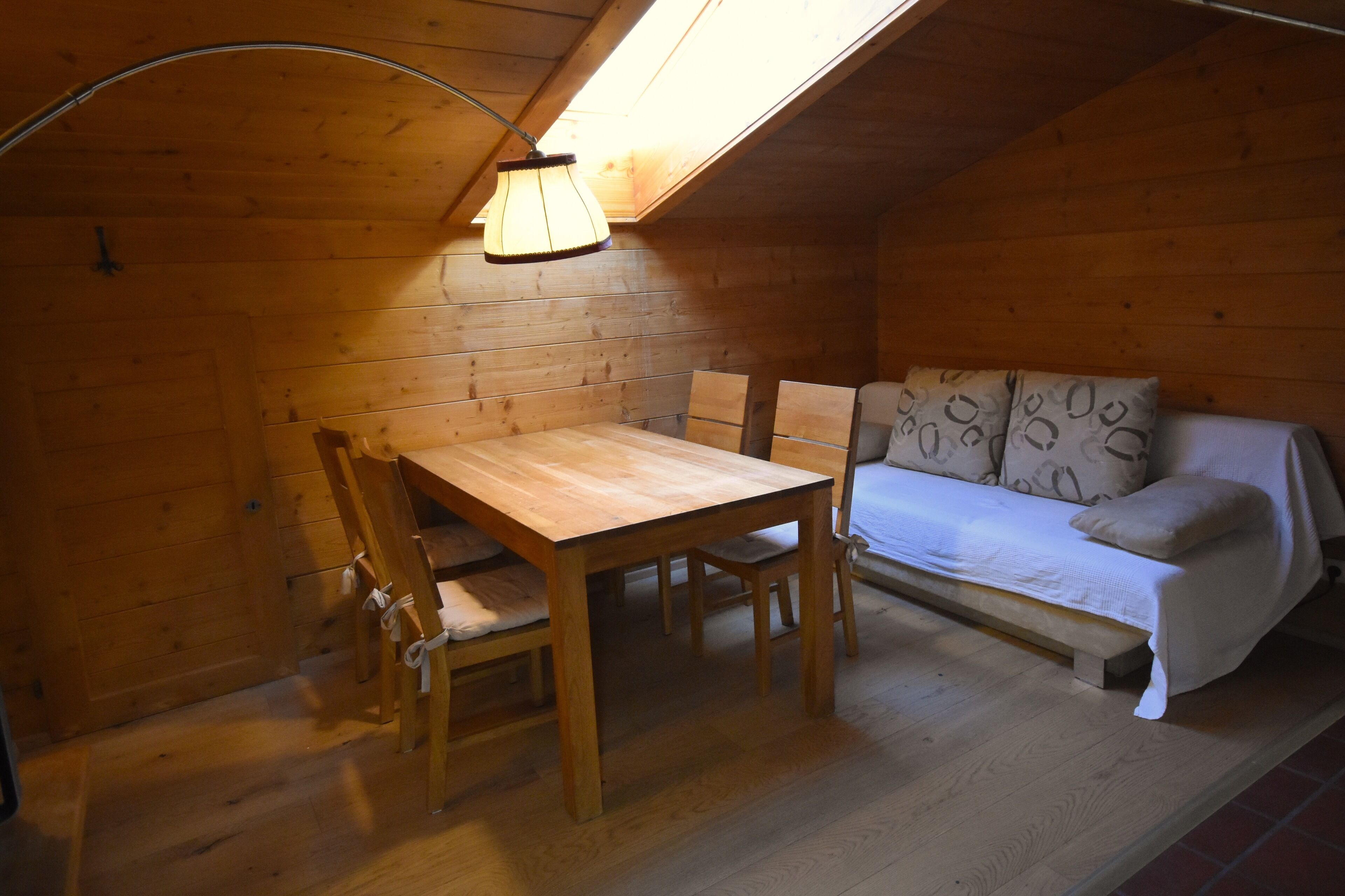 A cozy wooden room with a wooden table and chairs, a sofa, and a skylight above.