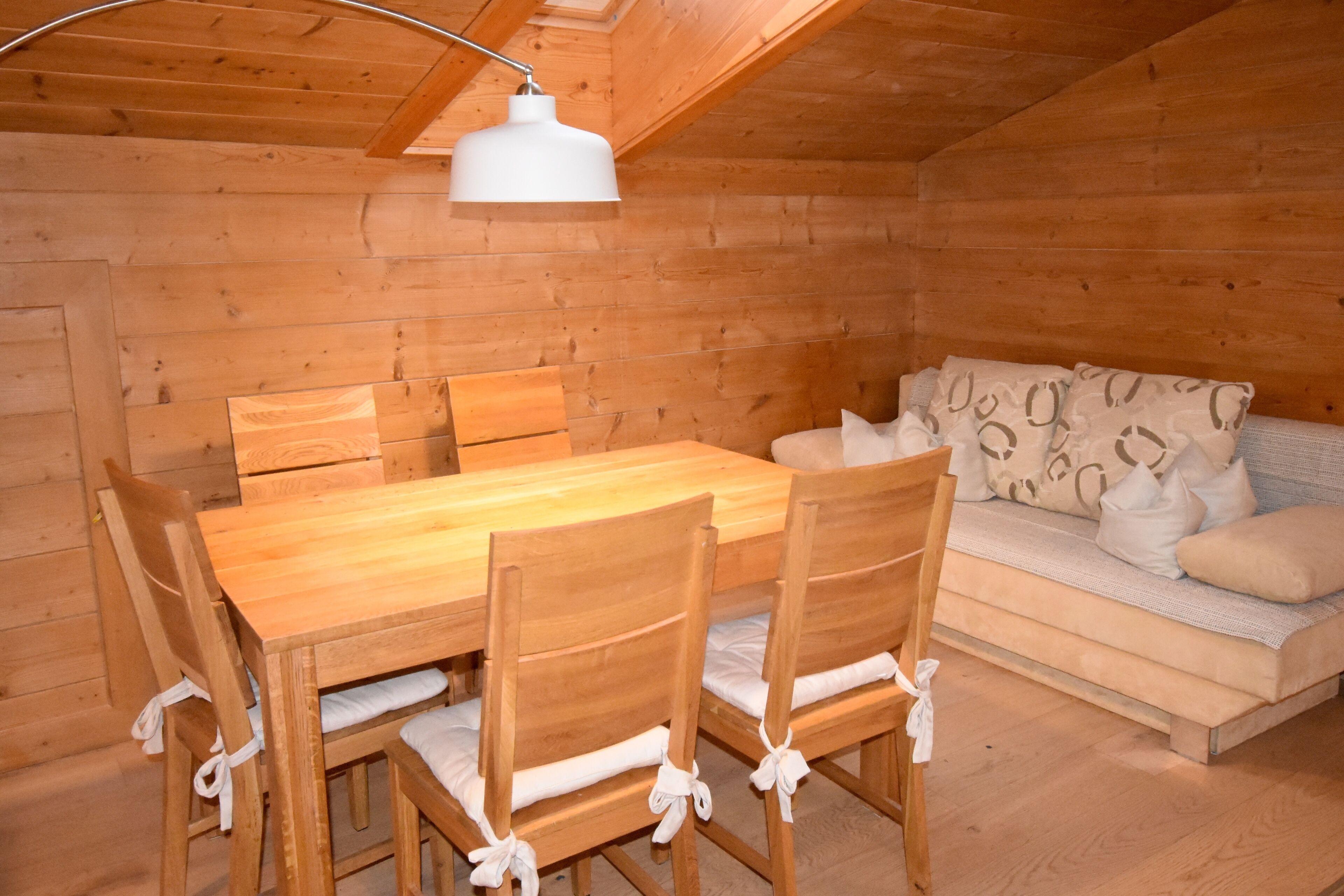 Interior de uma cabana de madeira com uma mesa de jantar, cadeiras e um sofá.