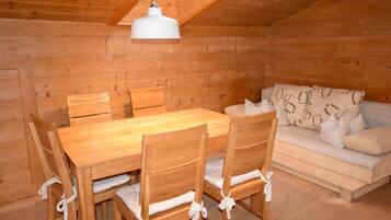Interior de uma cabana de madeira com uma mesa de jantar, cadeiras e um sofá.