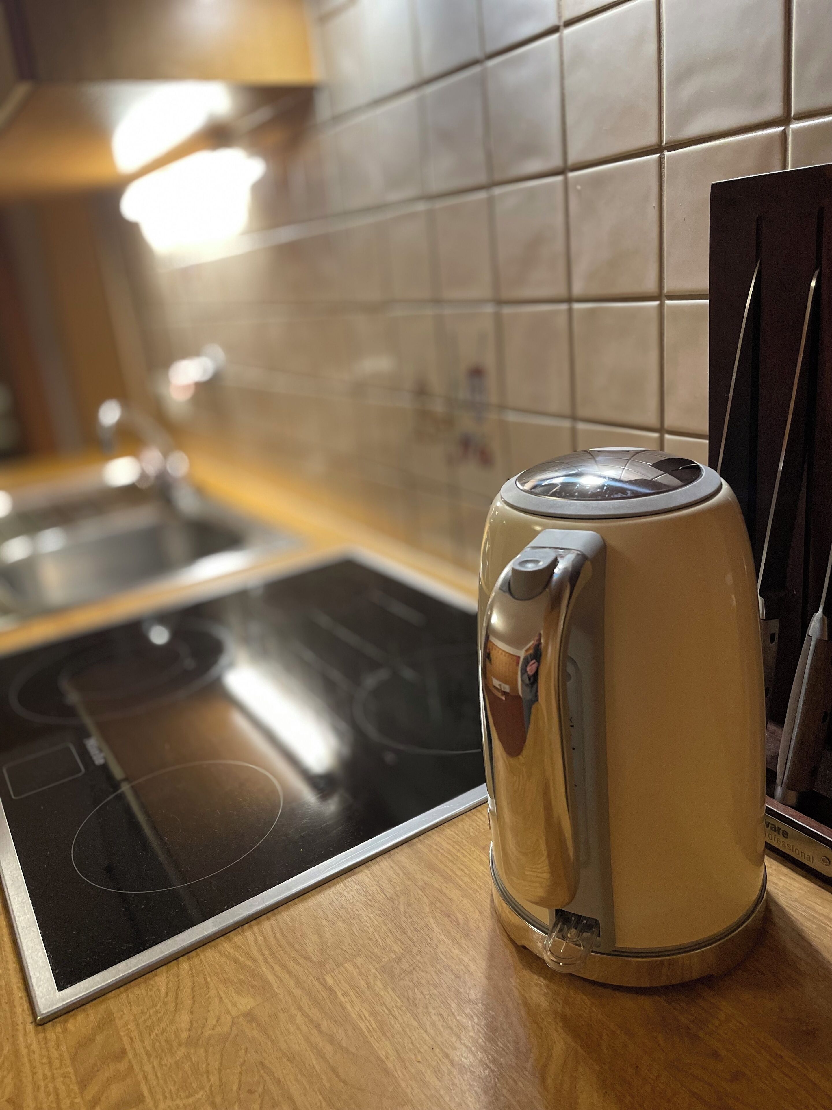 A kitchen with a stove, a kettle, and a tiled backsplash.