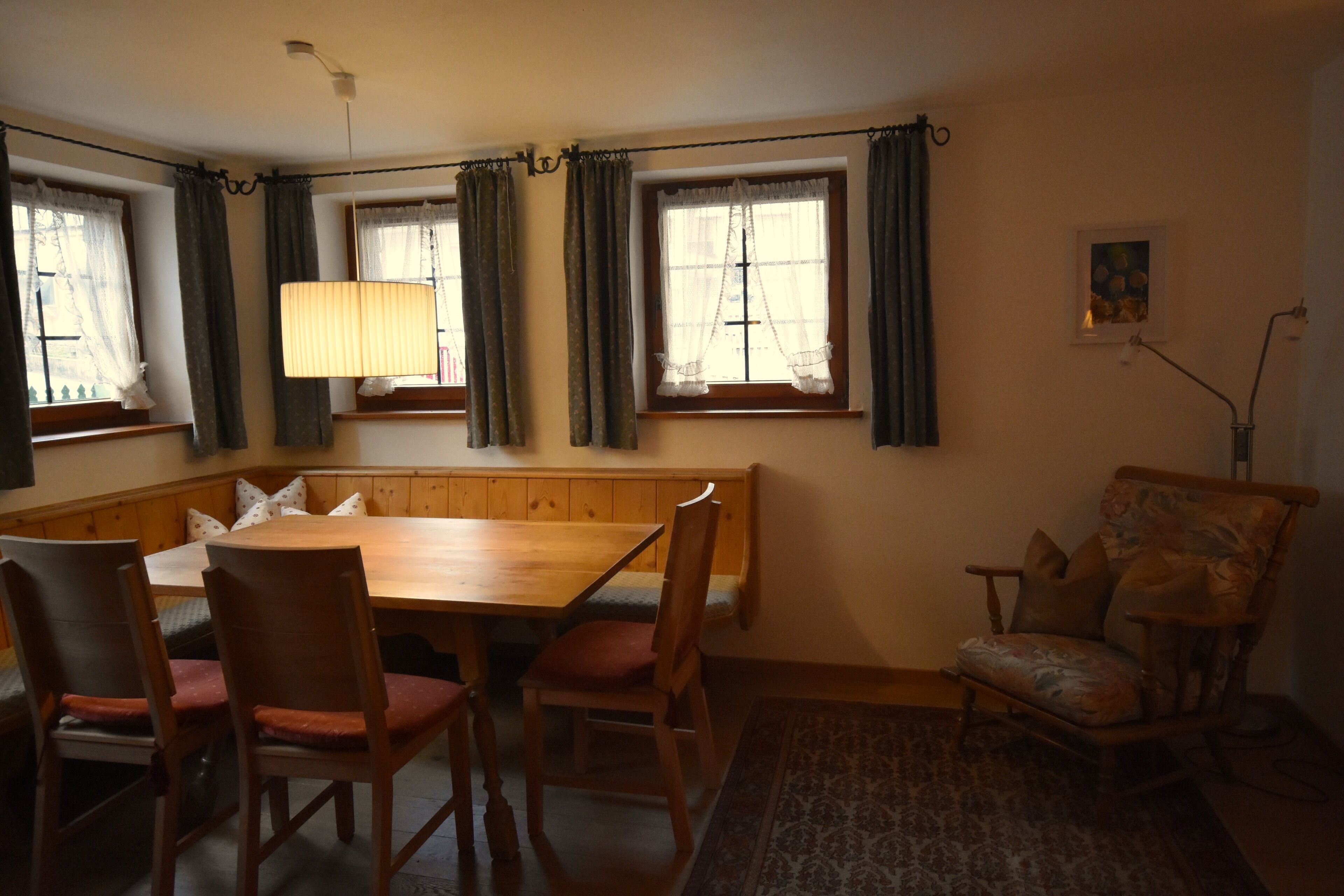 A dining area with a wooden table and chairs, a bench, and a patterned rug.