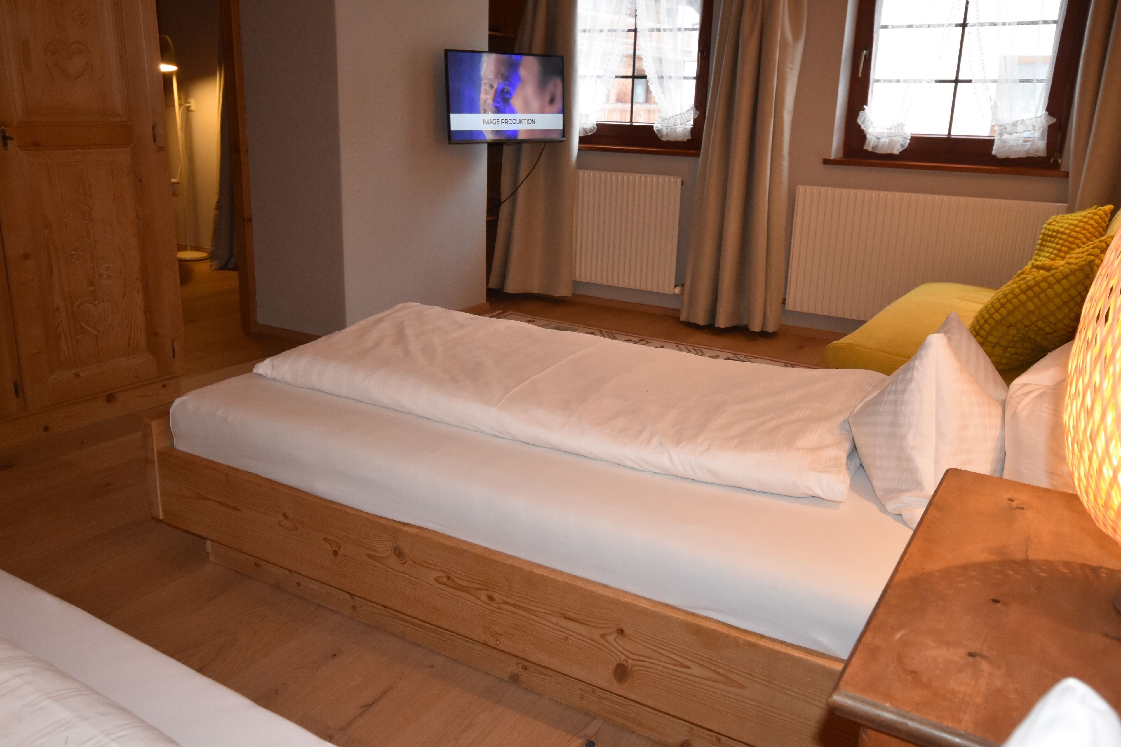 A bedroom with a wooden bed, a television on the wall, and a window with curtains.
