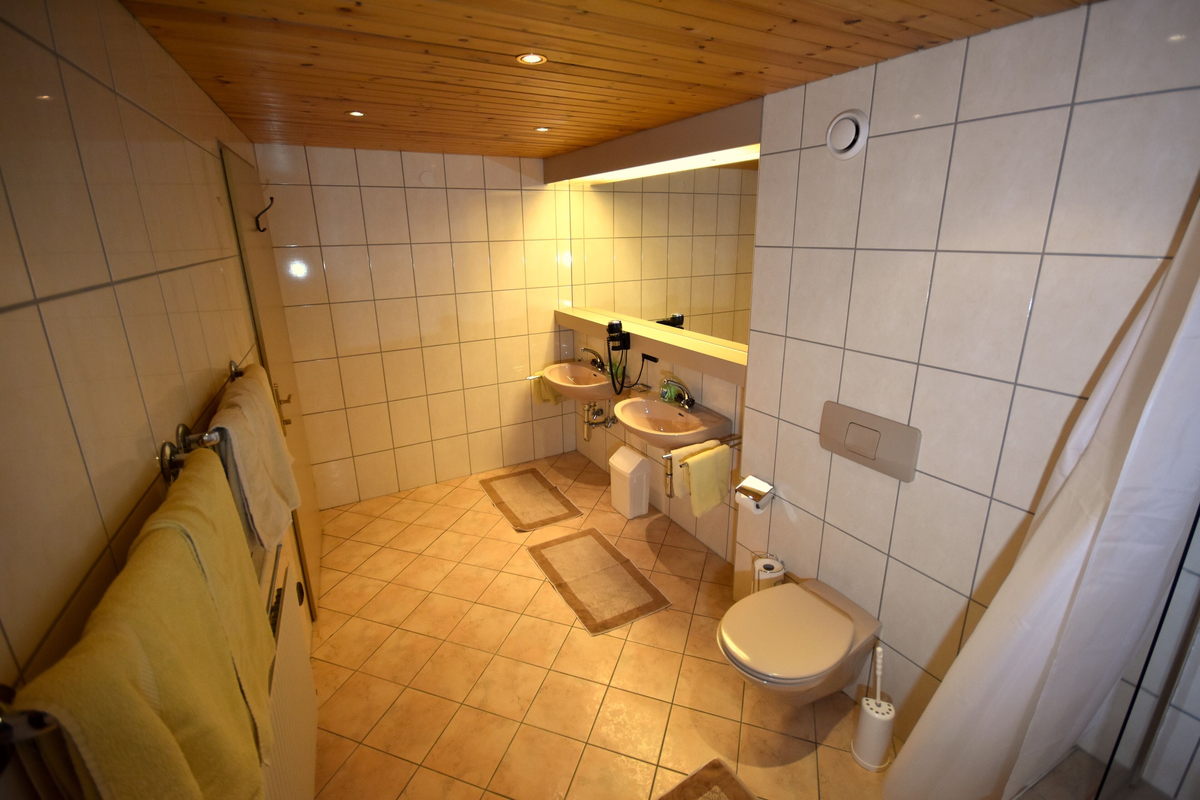 Un baño con techo de madera, dos lavamanos, un inodoro y un espejo.