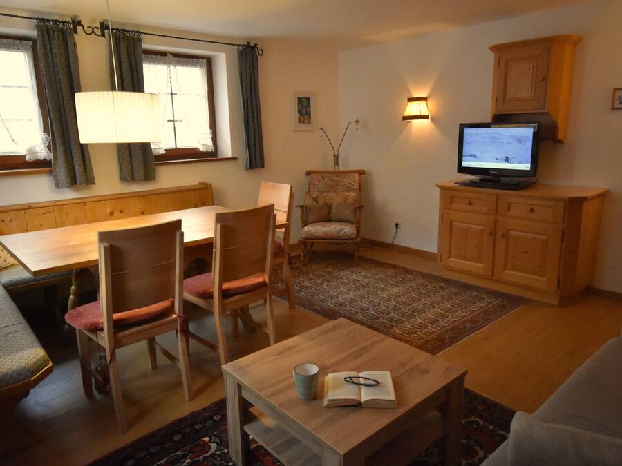 Ein gemütliches Wohnzimmer mit einem Holzespeisetisch, Stühlen, einer Couch, einem Fernseher und einem Schrank.