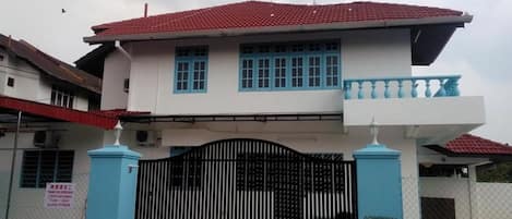 A two-story building with a red-tiled roof, a balcony with blue railings, and a black gate.