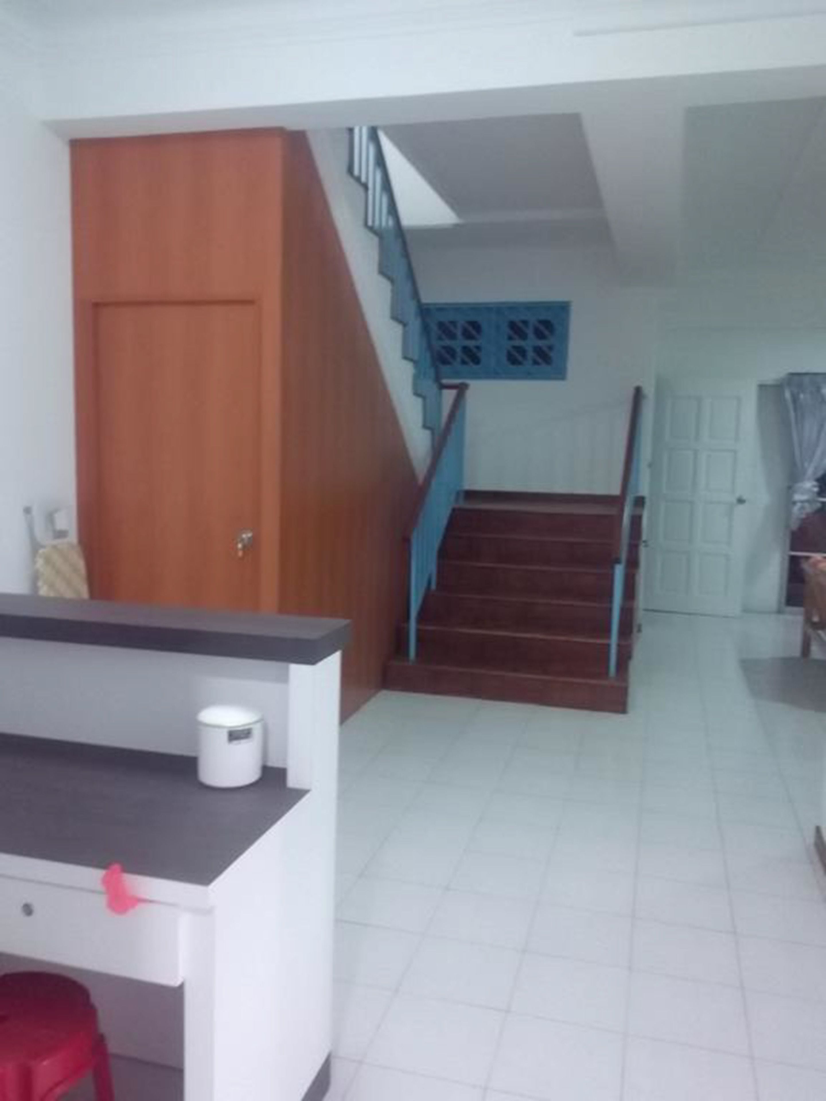 Une pièce avec une porte en bois, un bureau blanc avec une chaise rouge, un escalier avec des rampes bleues et un sol carrelé de blanc.