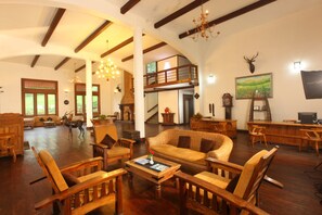 A spacious living room with wooden furniture, a fireplace, and a balcony. - The New Oak Fields (Devikolam)