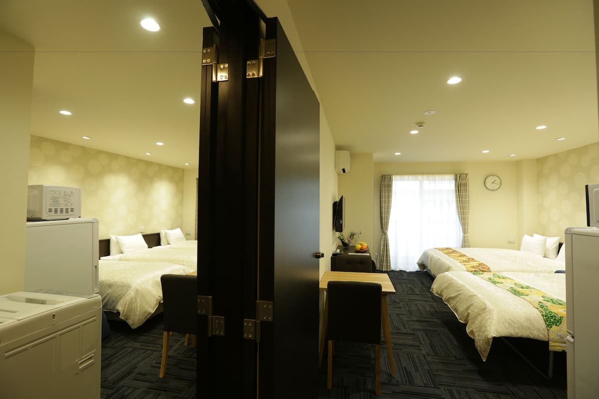 Habitación de hotel con dos camas, un escritorio, una silla, una lavadora y un reloj en la pared.