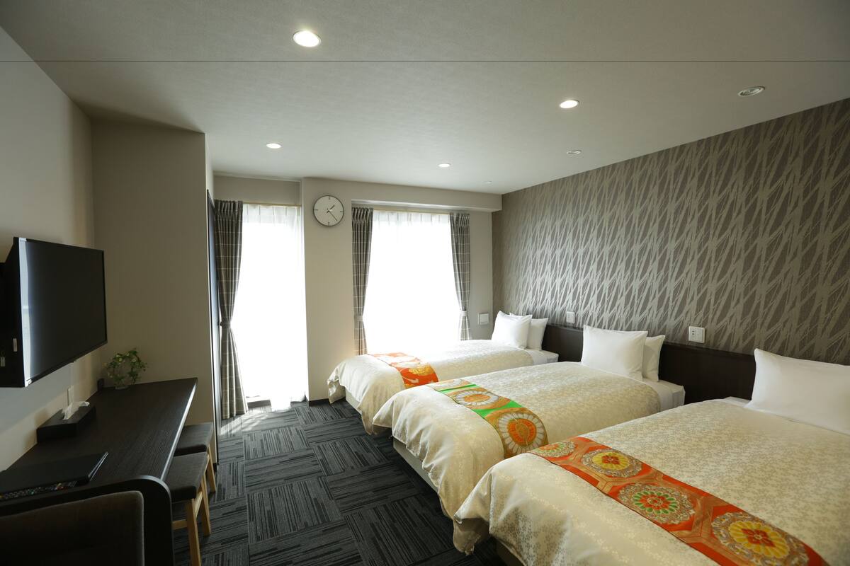 Habitación de hotel con dos camas, un escritorio, un televisor de pantalla plana y una ventana con cortinas.